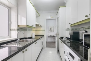 A compact kitchen with white cabinetry, a black countertop, and a built-in washing machine.