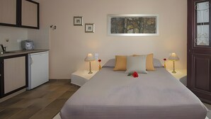 Ett hotellrum med en säng, sängbord, ett litet pentry och en tavla på väggen.