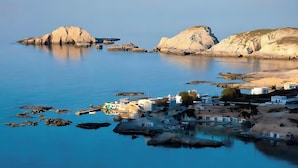 Un village côtier avec des bâtiments situés près de l’eau, des affleurements rocheux et un ciel dégagé.