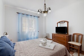 Un dormitorio con una cama, un aparador de madera, un televisor, una silla y una araña.
