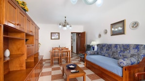 A living room with a wooden cabinet, a sofa, a dining table with chairs, and a checkered floor. - Apartment 'Dunamar' with Private Terrace, Wi-Fi and Air Conditioning (Castro Marim)