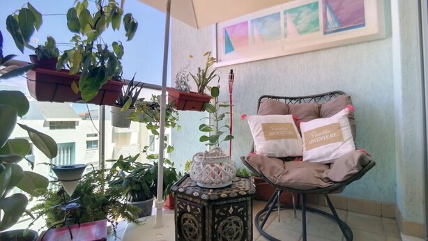 A balcony with potted plants, a chair with cushions, and a decorative item on a small table. - Apartment 'Athena' with Balcony, Wi-Fi and Air Conditioning (Monte Gordo)