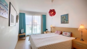 A hotel room with a bed, bedside lamps, a TV, a window with curtains, and artwork on the walls. - Apartment 'Athena' with Balcony, Wi-Fi and Air Conditioning (Monte Gordo)
