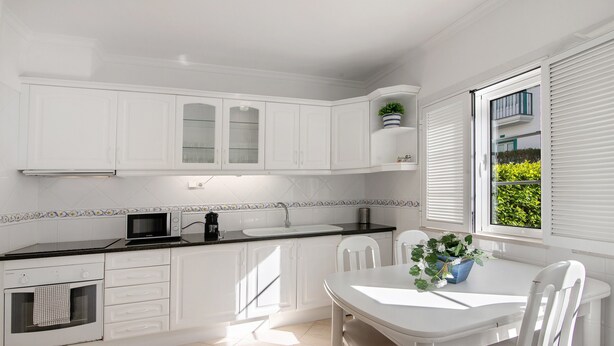 Una cocina moderna con armarios blancos, microondas, pileta y comedor con mesa y sillas.
