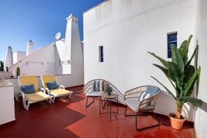 Eine Dachterrasse mit weißen Wänden, einem roten Boden und zwei Loungestühlen mit Kissen.