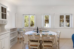Ein Essbereich mit einem runden Tisch, weißen Stühlen und einem Fenster mit Fensterläden.