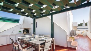 Terraza en la azotea con una mesa de comedor para cuatro, una parrilla y vistas a un edificio blanco con una torre.
