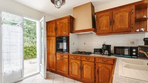 A kitchen with wooden cabinets, a gas stove, a microwave, and a sink. - Holiday Home 'Lumineuse Près La Rémigeasse' with Private Terrace, Private Garden and Wi-Fi (Dolus-d'Oléron)