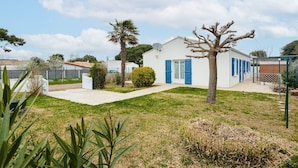 A white building with blue shutters, a paved driveway, and a small lawn with a palm tree. - Holiday Home 'Lumineuse Près La Rémigeasse' with Private Terrace, Private Garden and Wi-Fi (Dolus-d'Oléron)