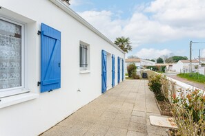Um edifício branco com persianas azuis, um caminho pavimentado estreito e um céu claro.