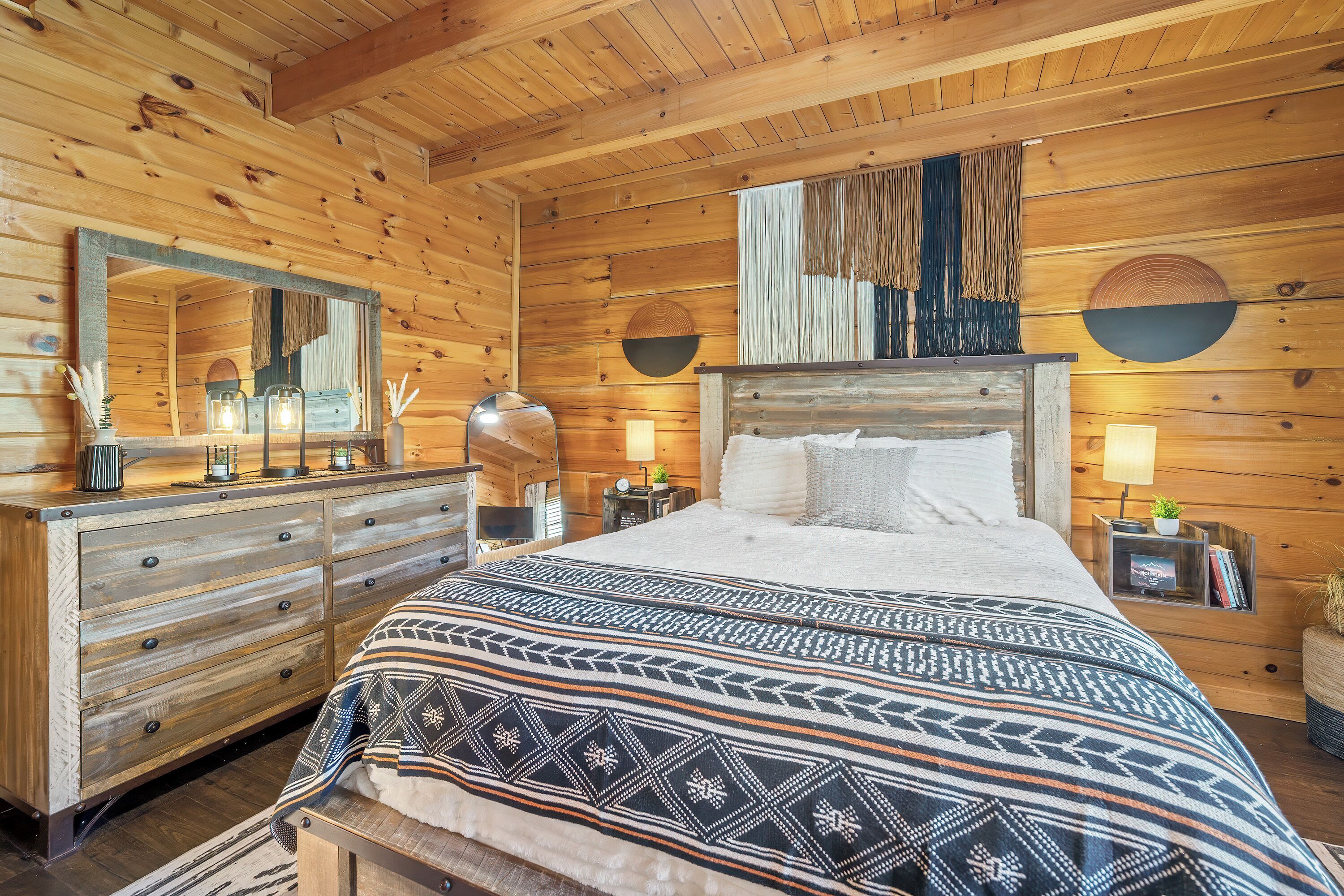 A wooden cabin bedroom with a bed, dresser, and mirror.
