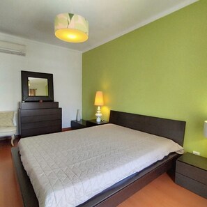 A bedroom with a bed, a dresser, a nightstand, a lamp, and a hanging light fixture.