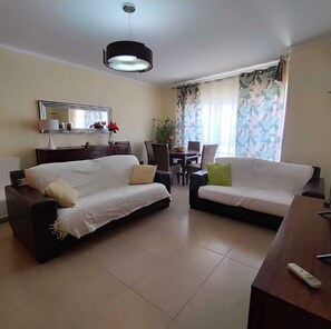 A hotel room with two sofas, a dining table, a TV, and a large window with curtains.