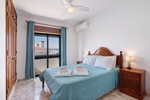 Une chambre d’hôtel avec un lit, une table de chevet, un ventilateur de plafond et une fenêtre avec des rideaux.