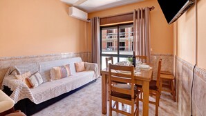 Una habitación con sofá, mesa de comedor, sillas, ventilador de techo y televisor montado en la pared.