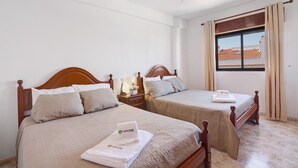 Una habitación de hotel con dos camas de madera, un ventilador de techo, una ventana con cortinas y una mesita de noche con lámpara.