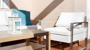 Een moderne buiten zithoek met een witte stoel, een houten tafel en een witte lantaarn.