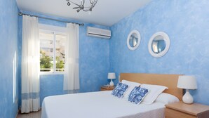 Een slaapkamer met een bed, twee nachtkastjes, een raam met gordijnen, een airconditioning en twee wandspiegels.