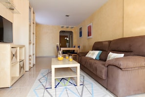 A living room with a brown sofa, a wooden coffee table, and a TV on a stand.