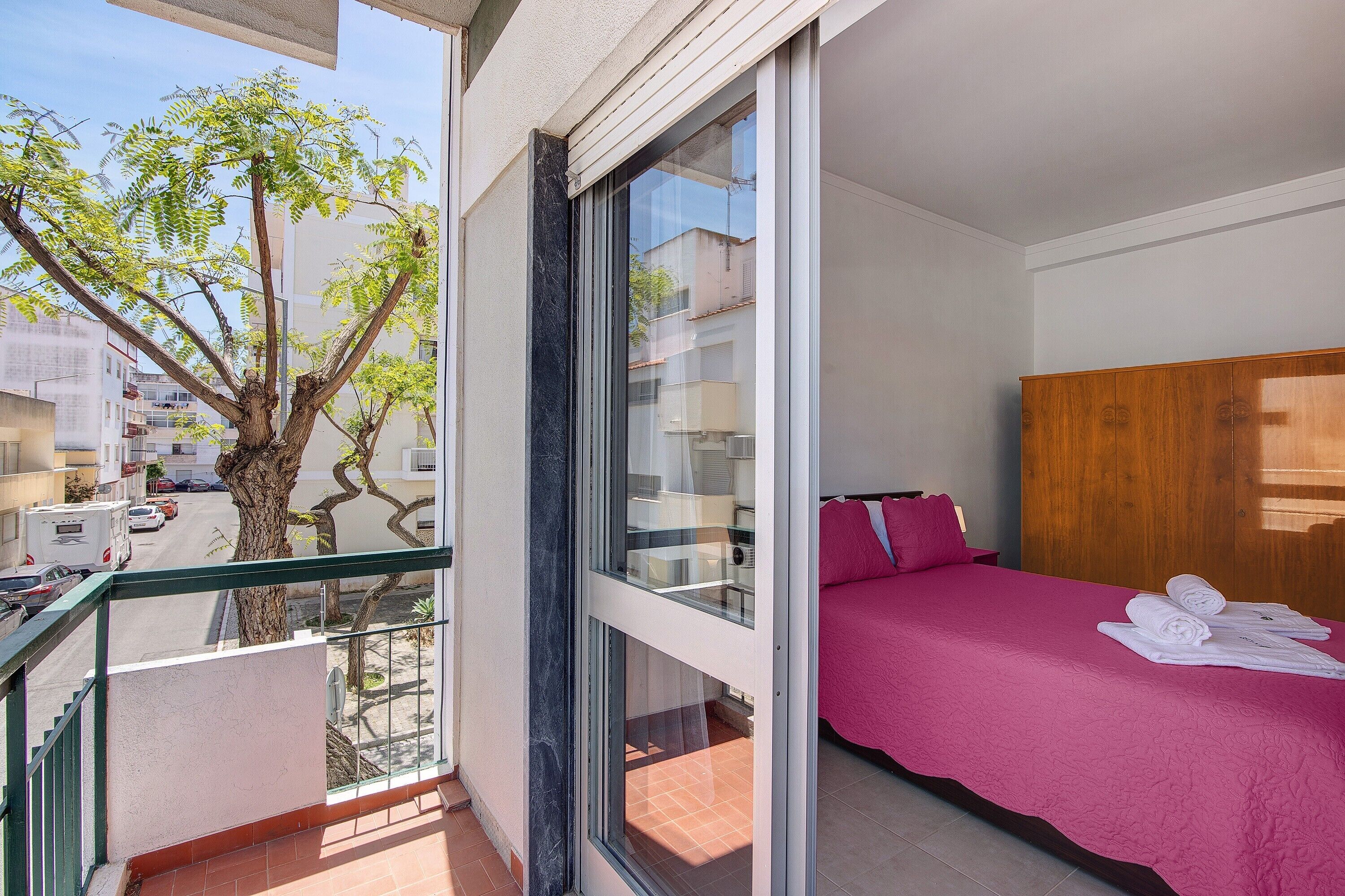 A bedroom with a bed, a window, a balcony, and a tree outside.