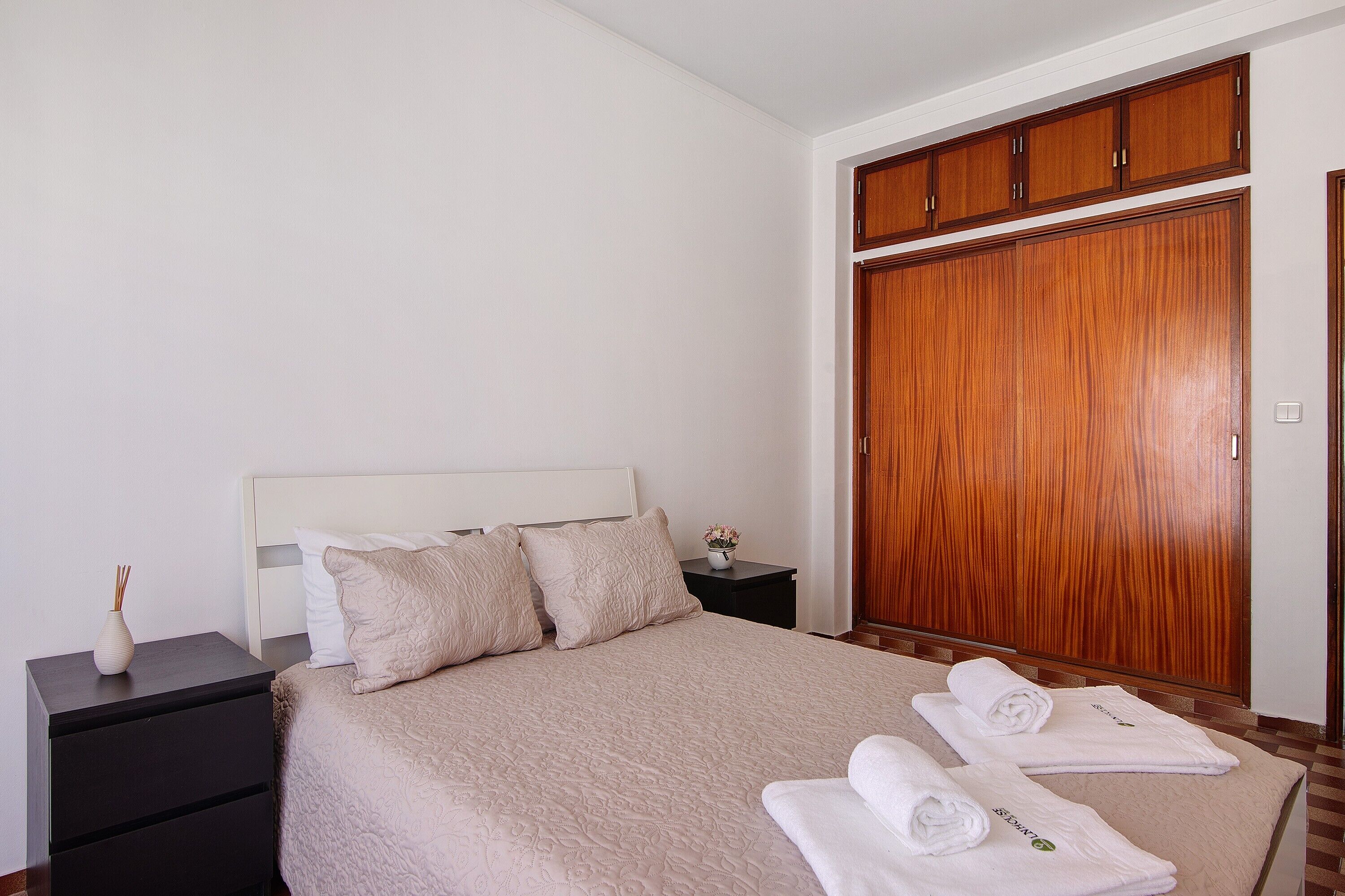 Une chambre à coucher avec un lit, une table de chevet, une armoire en bois et des serviettes sur le lit.