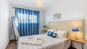 Ein Hotelzimmer mit Bett, Nachttisch, Lampe, einem Fenster mit Vorhängen und einer Wanduhr.