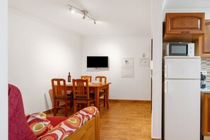 Un espace de vie compact comprenant un coin repas, un téléviseur fixé au mur et une cuisine équipée d’un four à micro-ondes et d’un réfrigérateur.