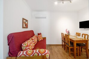 Une pièce avec un canapé rouge, une table à manger en bois avec des chaises, un téléviseur à écran plat et un climatiseur fixé au mur.