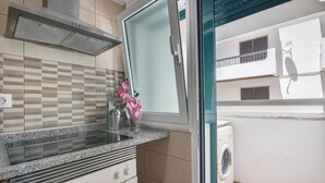Eine Küche mit Herd, Backofen und Mikrowelle, eine Glastür zu einem Balkon mit Waschmaschine und eine geflieste Spritzschutzwand.