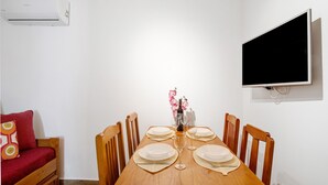 Ein Essbereich mit einem Holztisch, gedeckt für vier Personen, einem an der Wand montierten Fernseher und einer Klimaanlage über dem Tisch.