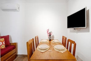 A dining area with a wooden table set for four, a TV mounted on the wall, and an air conditioning unit above the table. - Apartment 'Dourado' with Balcony, Wi-Fi and Air Conditioning (Monte Gordo)
