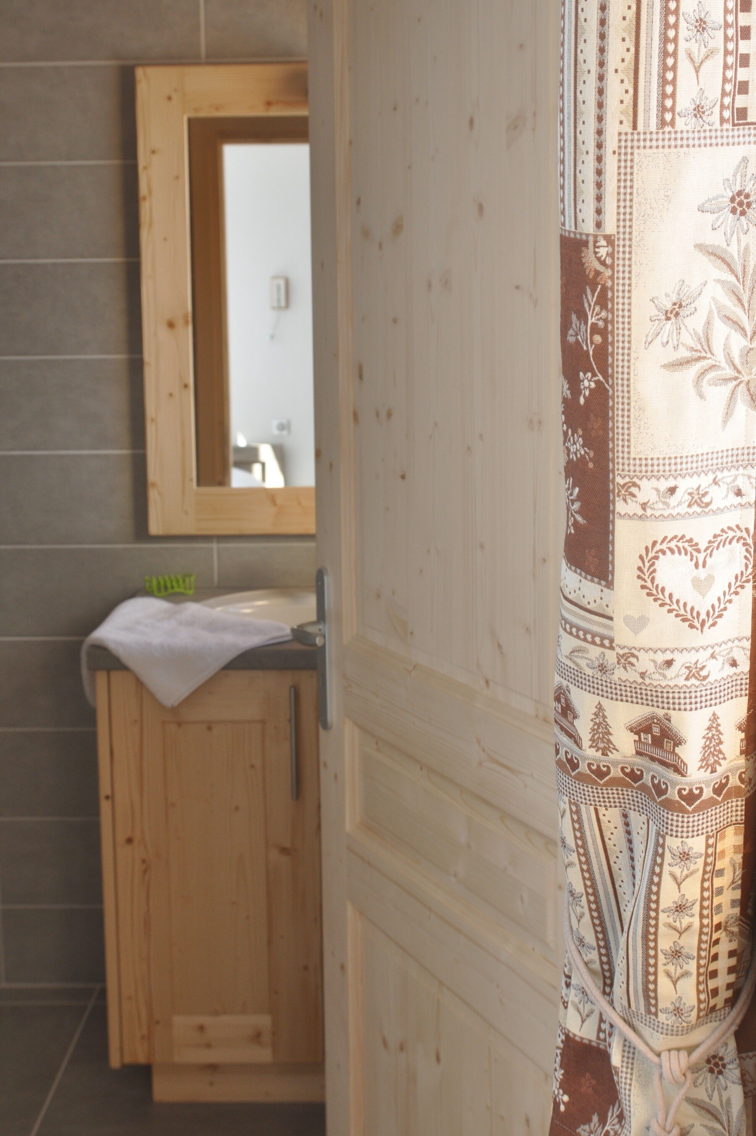 A bathroom with a wooden cabinet, a mirror, and a patterned curtain.