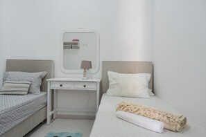 A bedroom with a bed, a bedside table with a mirror, a small desk, and a rolled-up towel.
