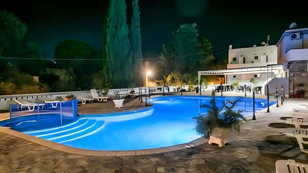 Piscina com espreguiçadeiras, um edifício com telhado plano e um céu noturno estrelado.