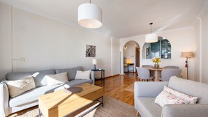 A modern living room with a grey sofa, a wooden coffee table, and a dining area with a table and chairs.