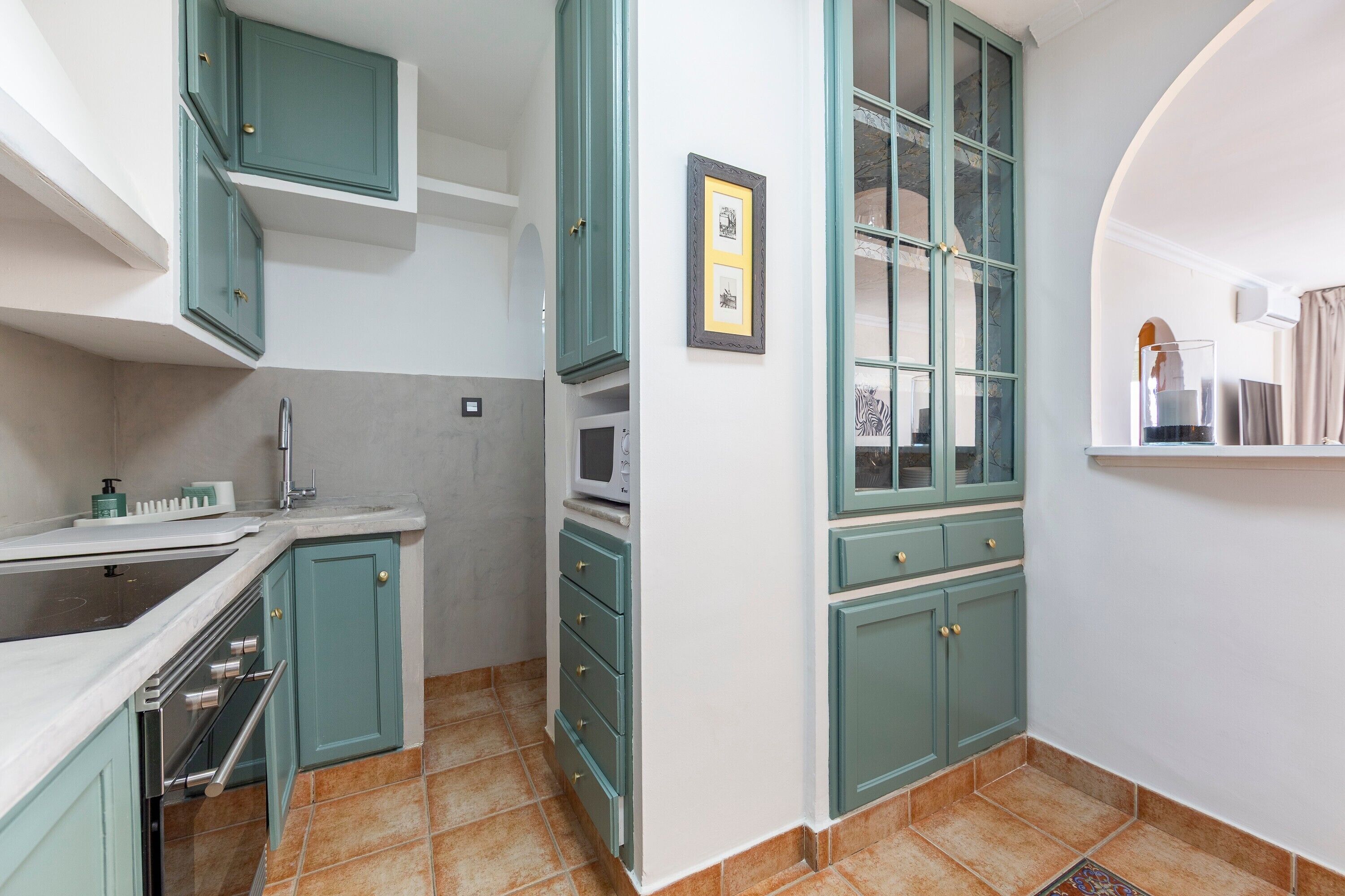 A kitchen with teal cabinets, a microwave, and a tiled floor.