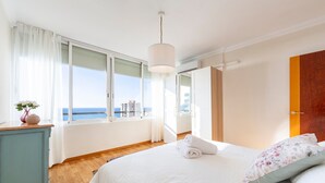 A bedroom with a large bed, a dresser, and a view of the sea.