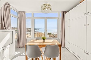 Una habitación con una mesa de comedor, dos sillas, una planta en maceta y vistas al mar.