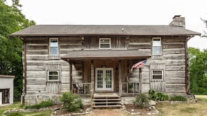 A rustic log cabin with a welcoming porch, a stone foundation, and an American flag.