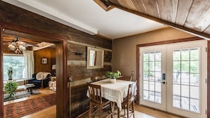 A rustic interior with a wooden dining table, a sofa, and a large window.