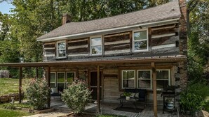 Eine zweistöckige Blockhütte mit überdachter Veranda, Sitzgelegenheiten im Freien und Grillplatz.