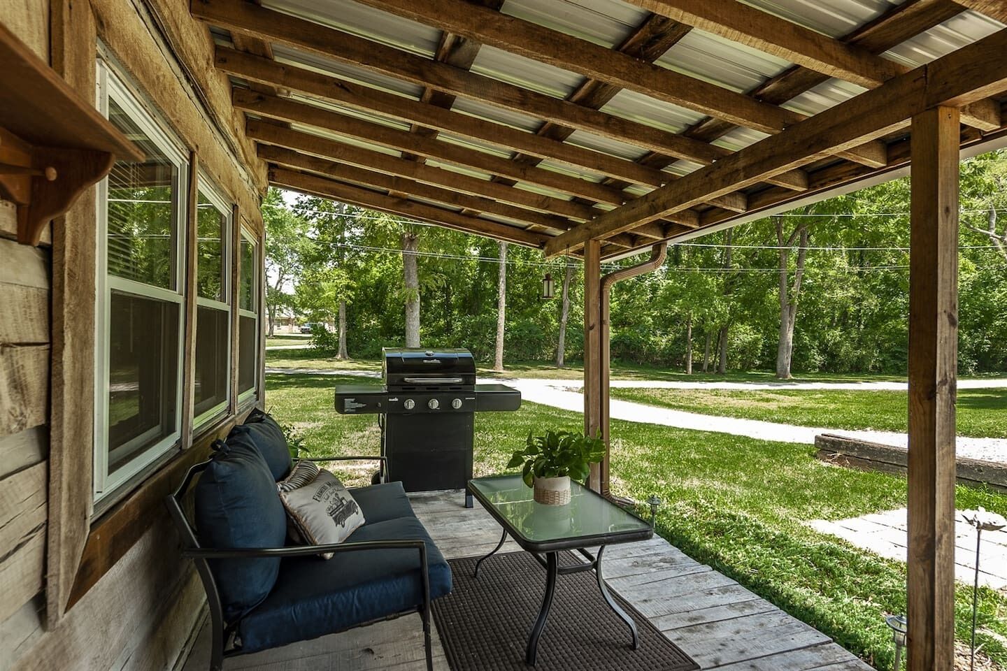 A covered patio with a grill, a sofa, and a small table.