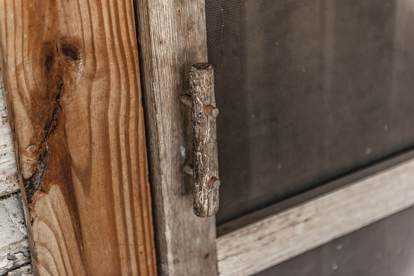 Een houten deur met een metalen grendel en een gaasraam.