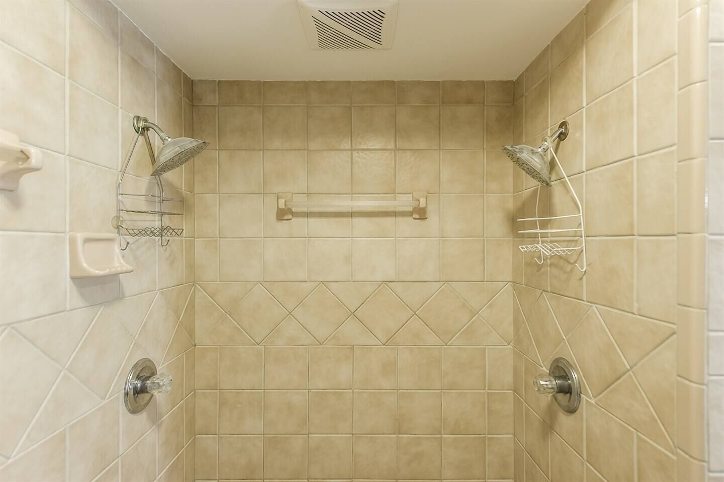 A shower with a handheld showerhead and a wall-mounted showerhead, a towel rack, and a shower control panel.