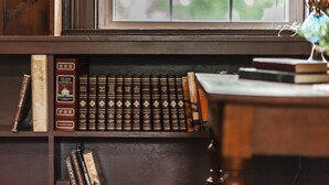 A bookshelf with a collection of books, a lamp, and a window with a view of greenery.