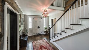 A hallway with a wooden floor, a red patterned rug, a chandelier, and a staircase with white railings.