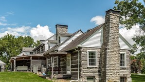 A log cabin with a stone chimney, a porch, and a garage.