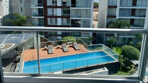 En modern byggnad med en pool på taket, glasräcken och flera balkonger.
