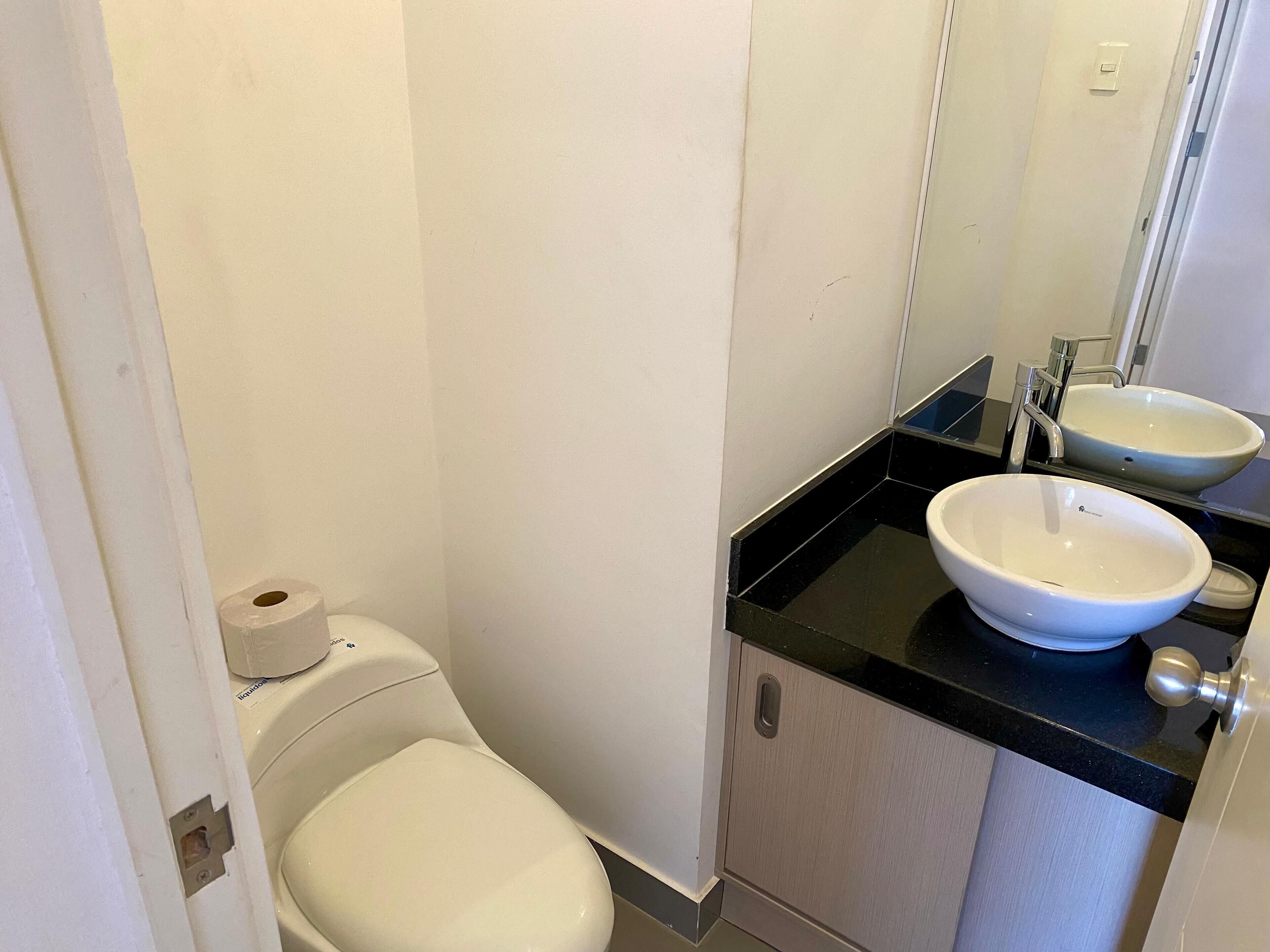 Un baño pequeño con inodoro, dos lavamanos y espejo.