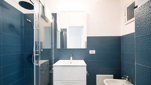 A bathroom with a glass shower enclosure, a white vanity with a sink, and a bidet. - WePuglia - Donna Simona (Polignano a Mare)